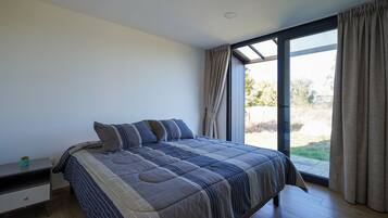 A bedroom with a large bed, a nightstand, a window with curtains, and a view of the outdoors.