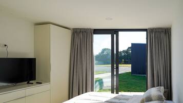 A bedroom with a bed, a TV on a stand, and a view of a grassy area through a sliding door.