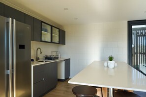 A modern kitchen with a built-in refrigerator, dark cabinetry, a white countertop, and a small plant on the island. - Oceana Suites Las Tranqueras (Puerto Varas)
