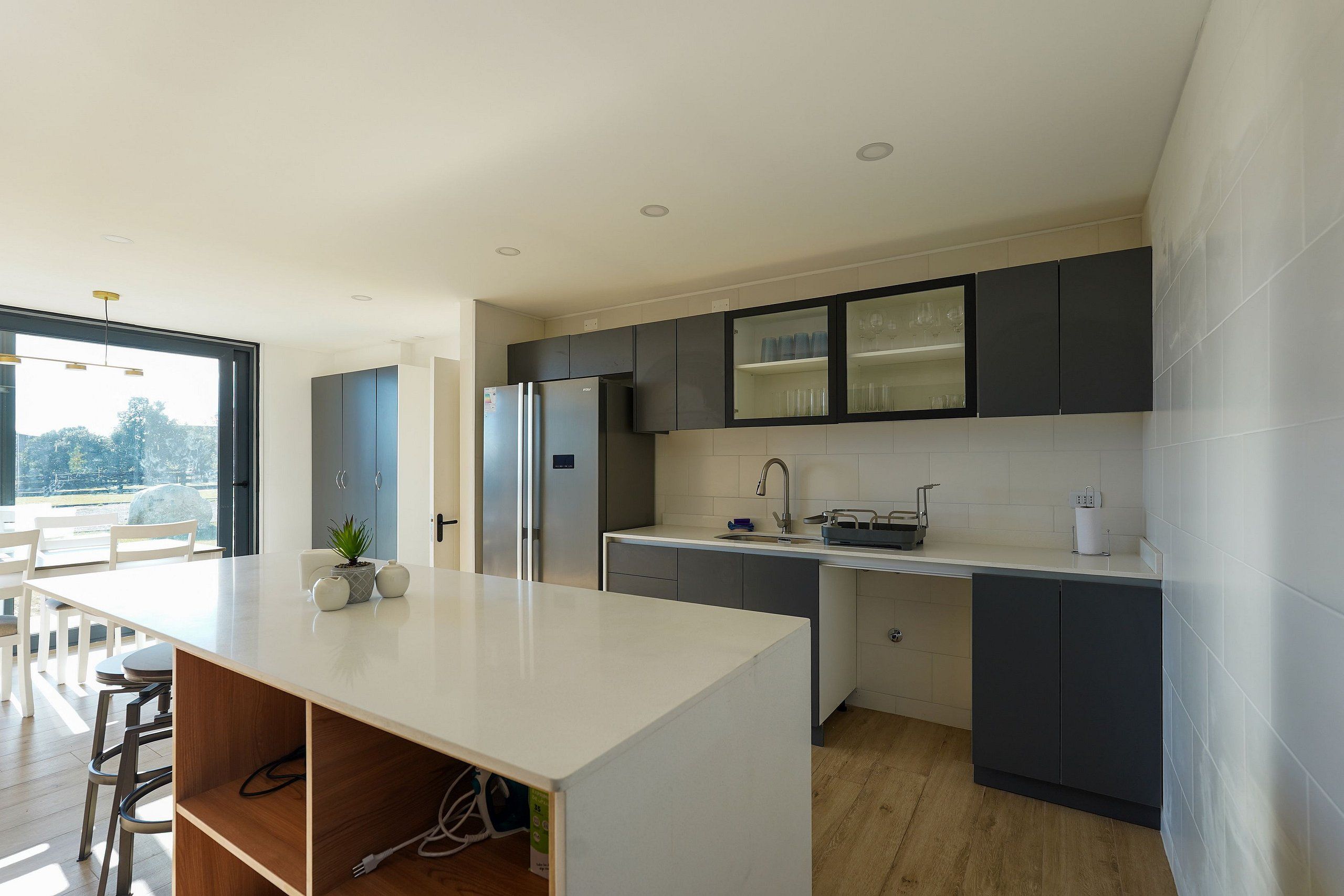 A modern kitchen with a central island, dark cabinets, and a large window.