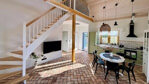 Un vaste espace de vie comprenant un escalier en bois, une table à manger avec des chaises, et un coin cuisine avec des placards et un évier.