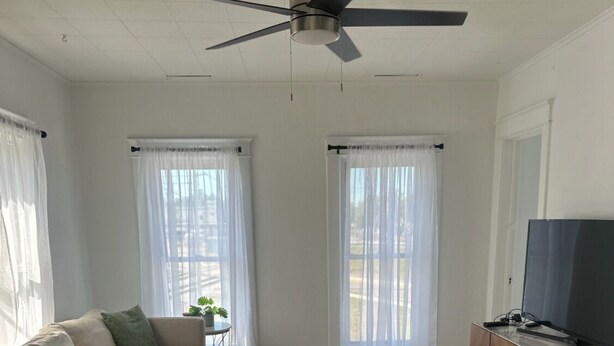A living room with a sofa, a glass coffee table, a TV, and a ceiling fan. - 4 bedroom beautiful modern apartment near Data center fully furnished  (Michigan City)