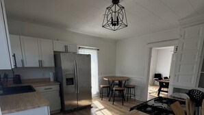 A modern kitchen with white cabinets, a stainless steel refrigerator, a wooden dining table, and a black gas stove. - 4 bedroom beautiful modern apartment near Data center fully furnished  (Michigan City)