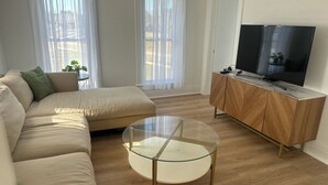 A living room with a sofa, a glass coffee table, a TV, and a wooden cabinet. - 4 bedroom beautiful modern apartment near Data center fully furnished  (Michigan City)