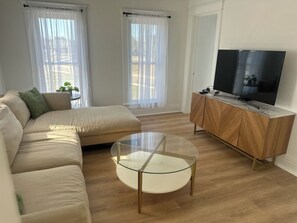 A living room with a sofa, a glass coffee table, a TV, and a wooden cabinet.