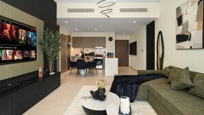 Una sala de estar moderna con televisor de pantalla plana, un sofá, una mesa de centro y un comedor al fondo.