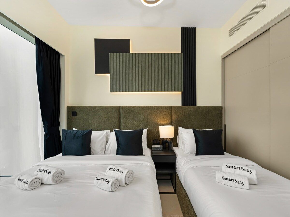 A hotel room with two beds, a nightstand, a lamp, and a headboard with a built-in shelf.