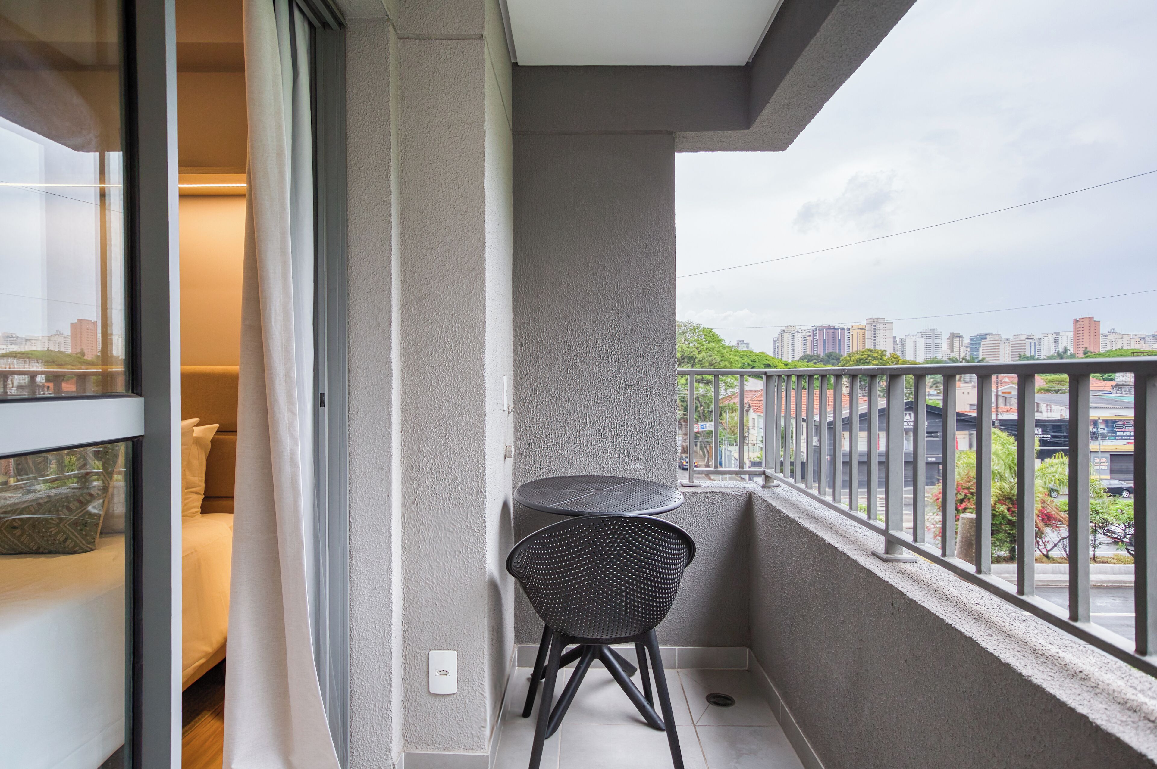 Un balcón con una pequeña mesa y silla, vistas de la ciudad y una puerta de cristal que da a una habitación.