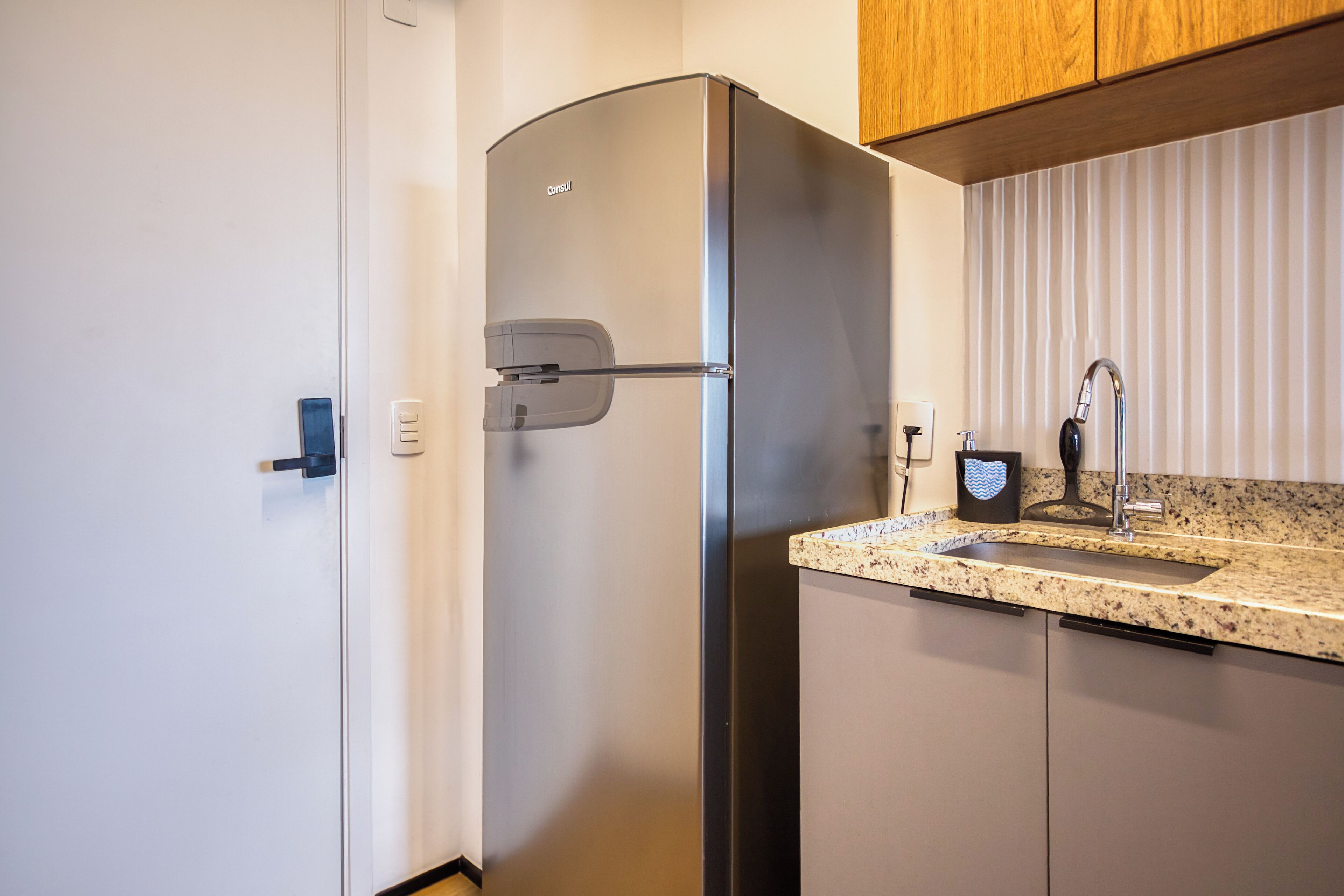 A compact kitchen with a built-in refrigerator, a granite countertop, and a stainless steel sink.