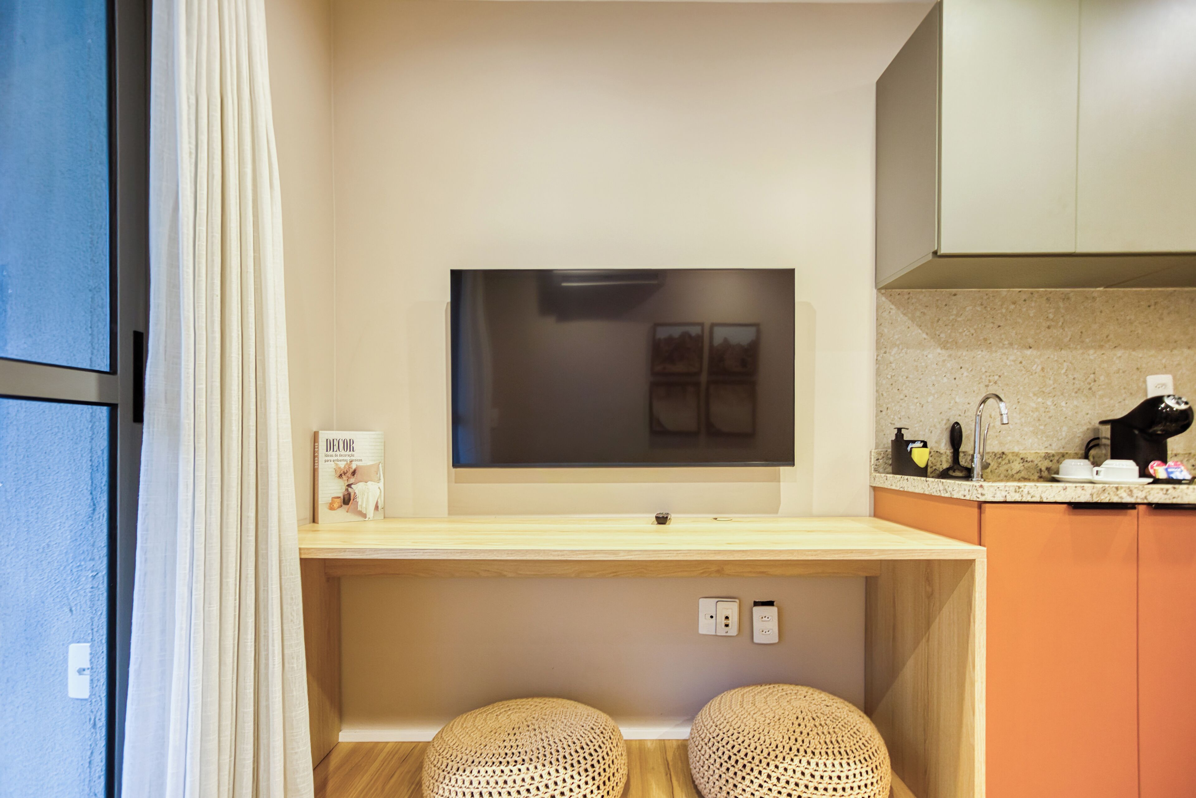 Een moderne keuken met een flatscreen televisie boven een houten aanrecht, twee geweven krukken en een granieten spatwand.