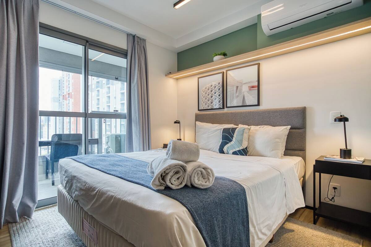 Ein Hotelzimmer mit einem großen Bett, einem Schreibtisch, einem Stuhl, einem Fenster mit Vorhängen und zwei gerahmten Bildern an der Wand.