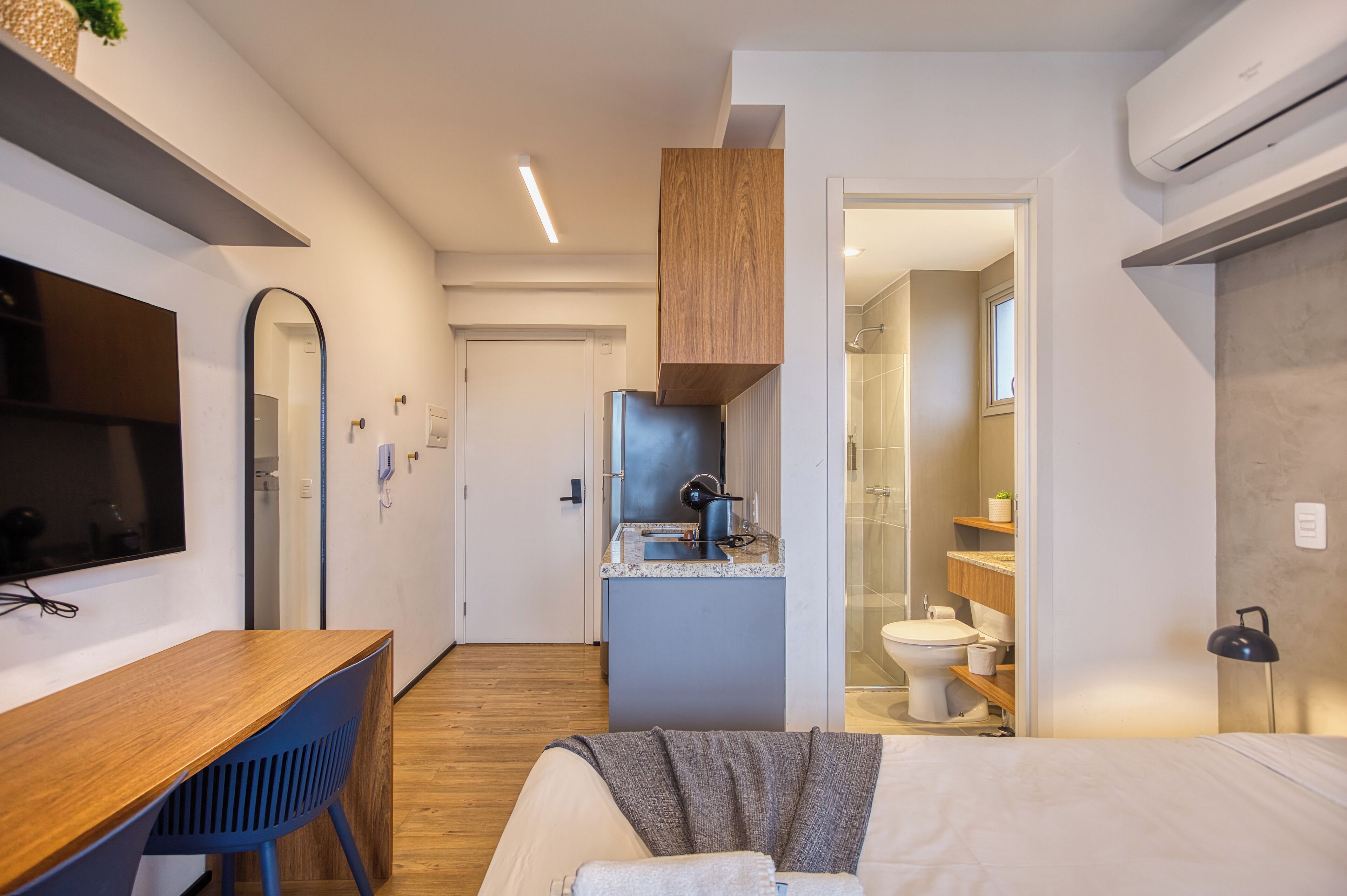 Een moderne hotelkamer met een houten bureau, een bed, een kleine kitchenette en een badkamer.