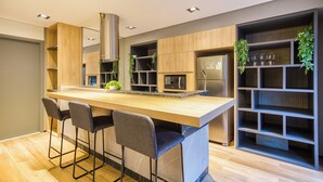 A modern kitchen with a central island, bar stools, built-in appliances, and a shelving unit with plants.