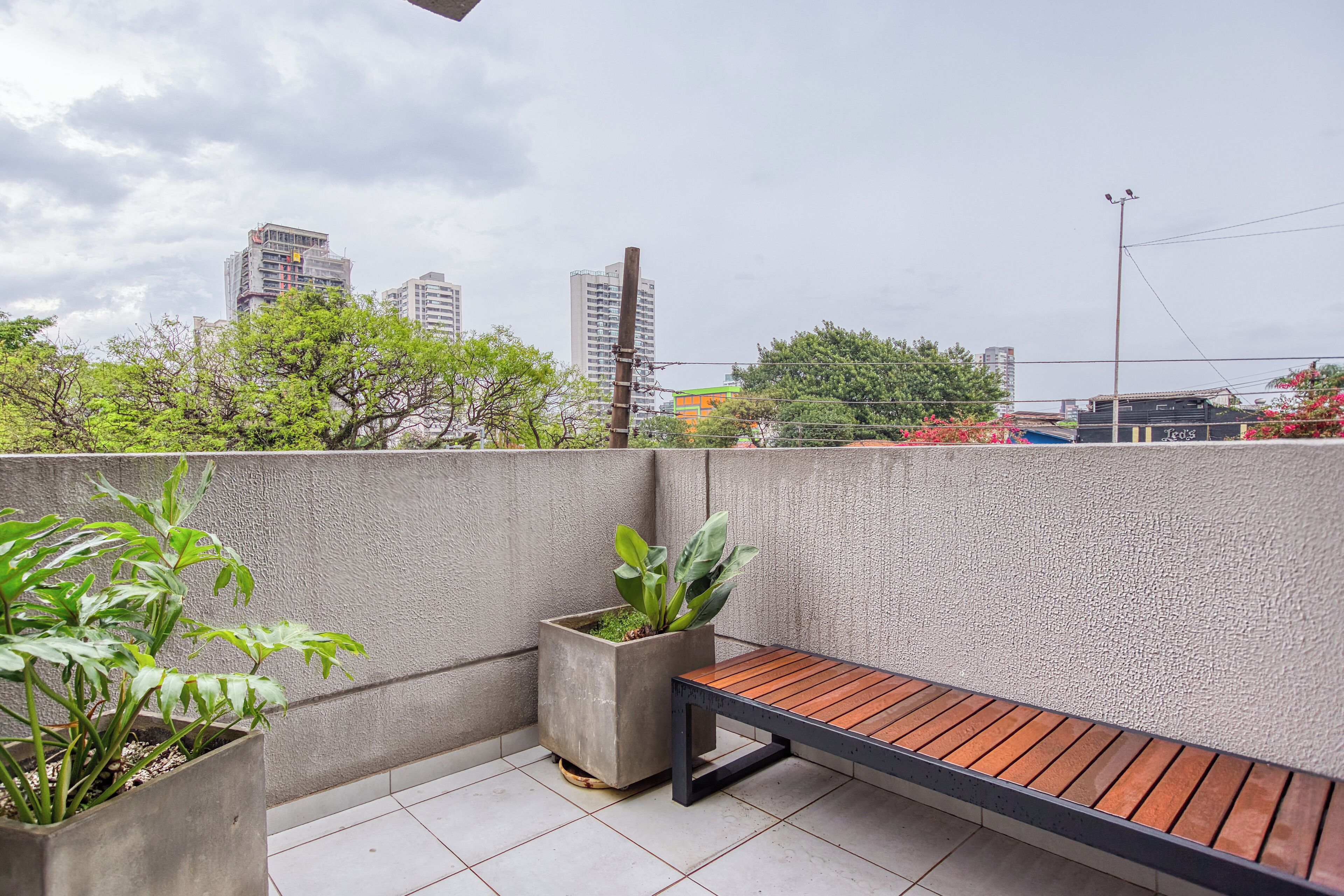 Un balcón con banca de madera, dos plantas en macetas y vista a la ciudad.