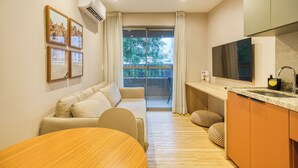 A modern living room with a sofa, a dining table, and a kitchen area with a TV and sink.