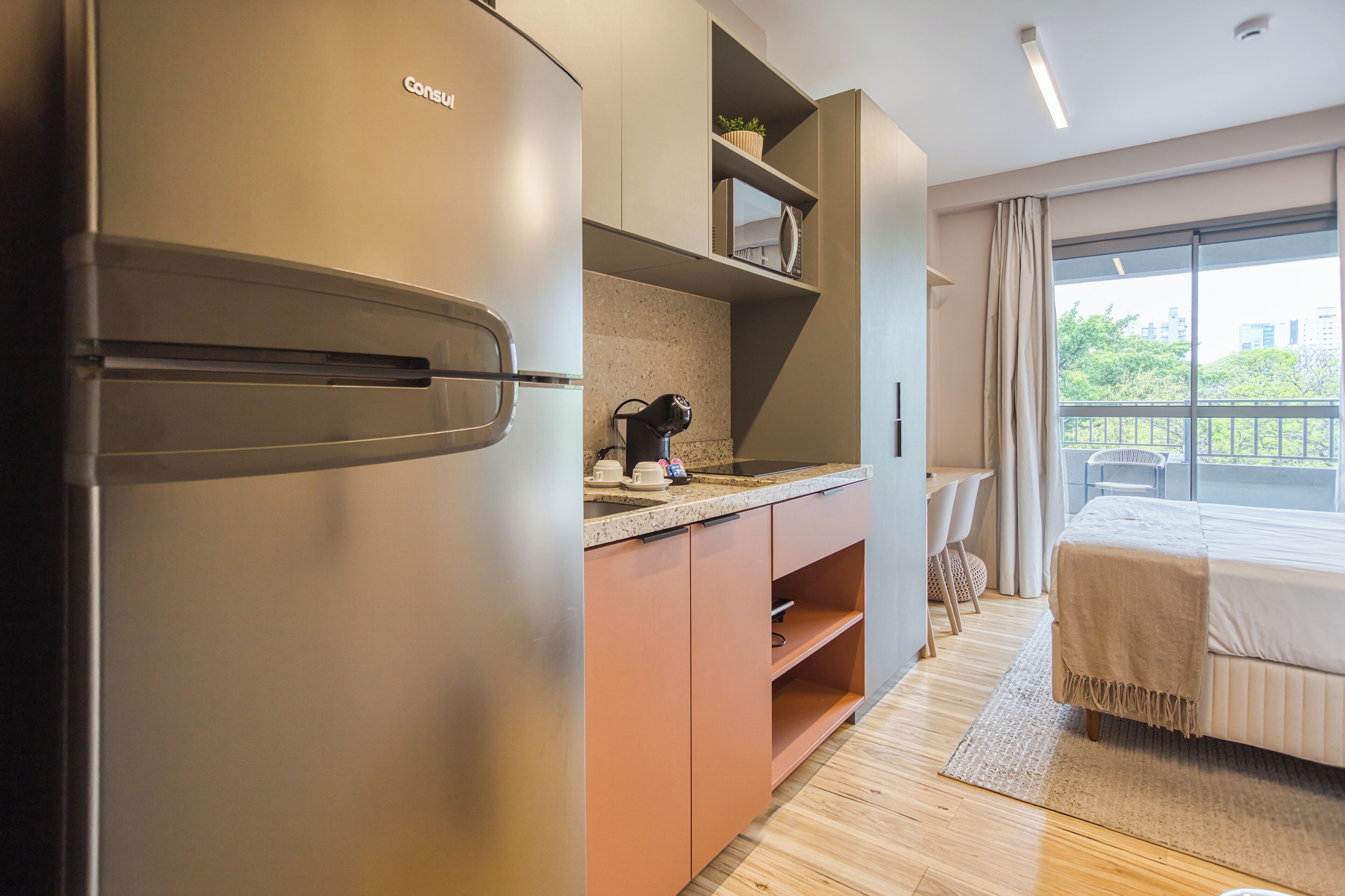 A modern hotel room with a kitchenette, a bed with a view, and a balcony.