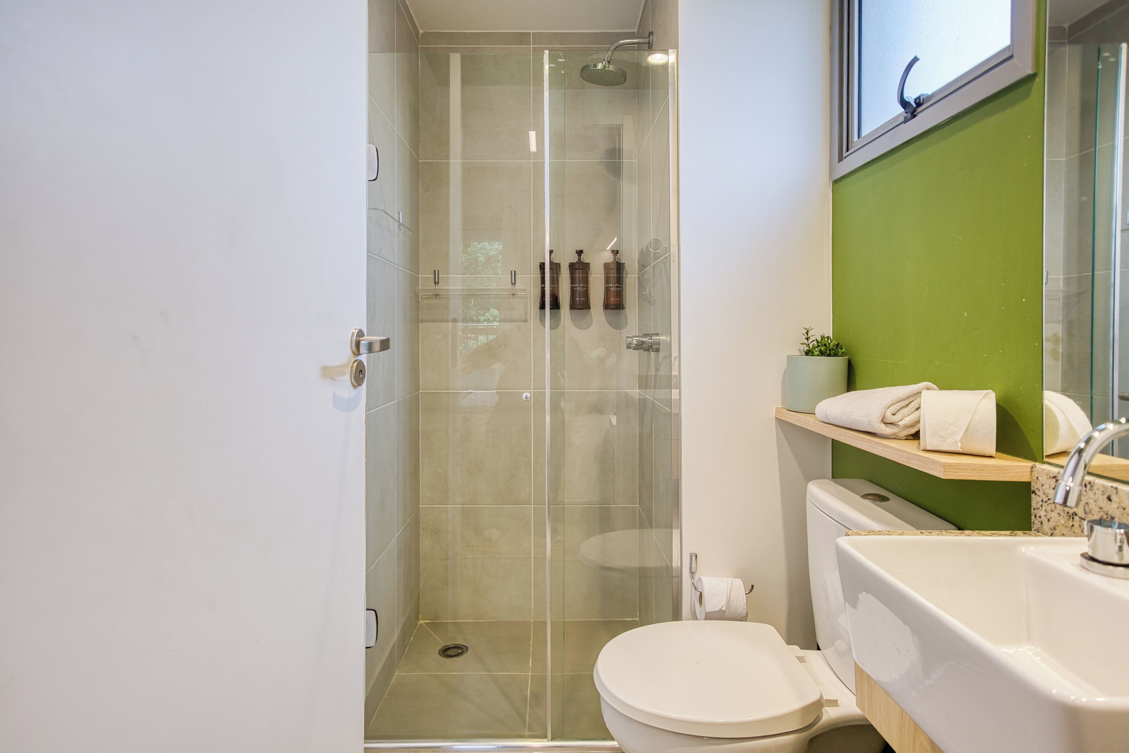 Et moderne badeværelse med en brusekabine med glasvægge, et hvidt toilet, en vask og en grøn accentvæg.