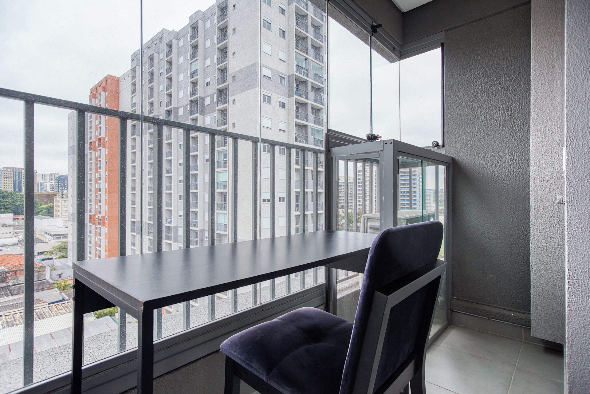 A balcony with a table and chair, offering a view of high-rise buildings.