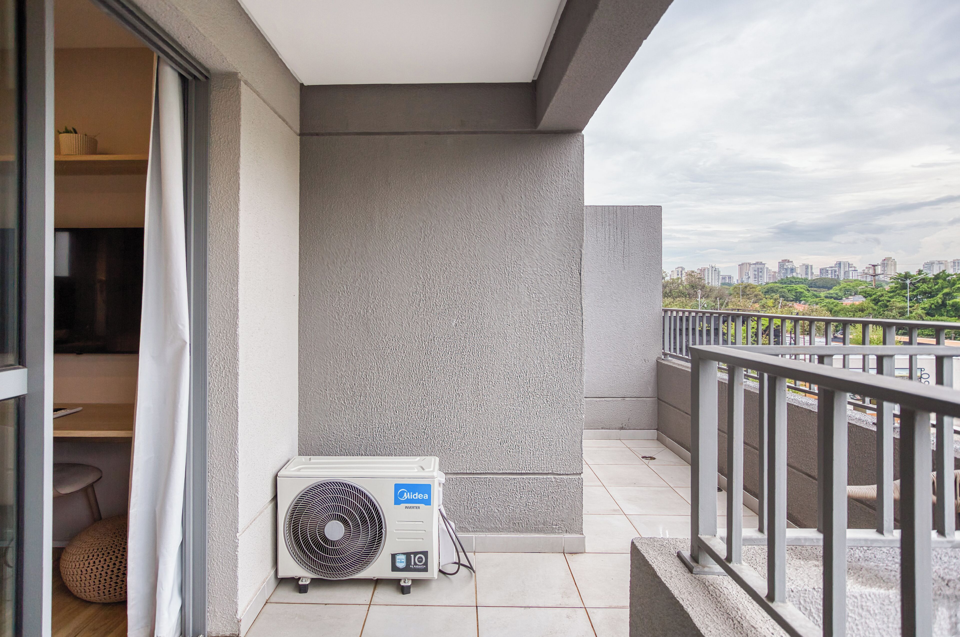 A balcony with a white air conditioning unit, a view of a cityscape, and a railing.
