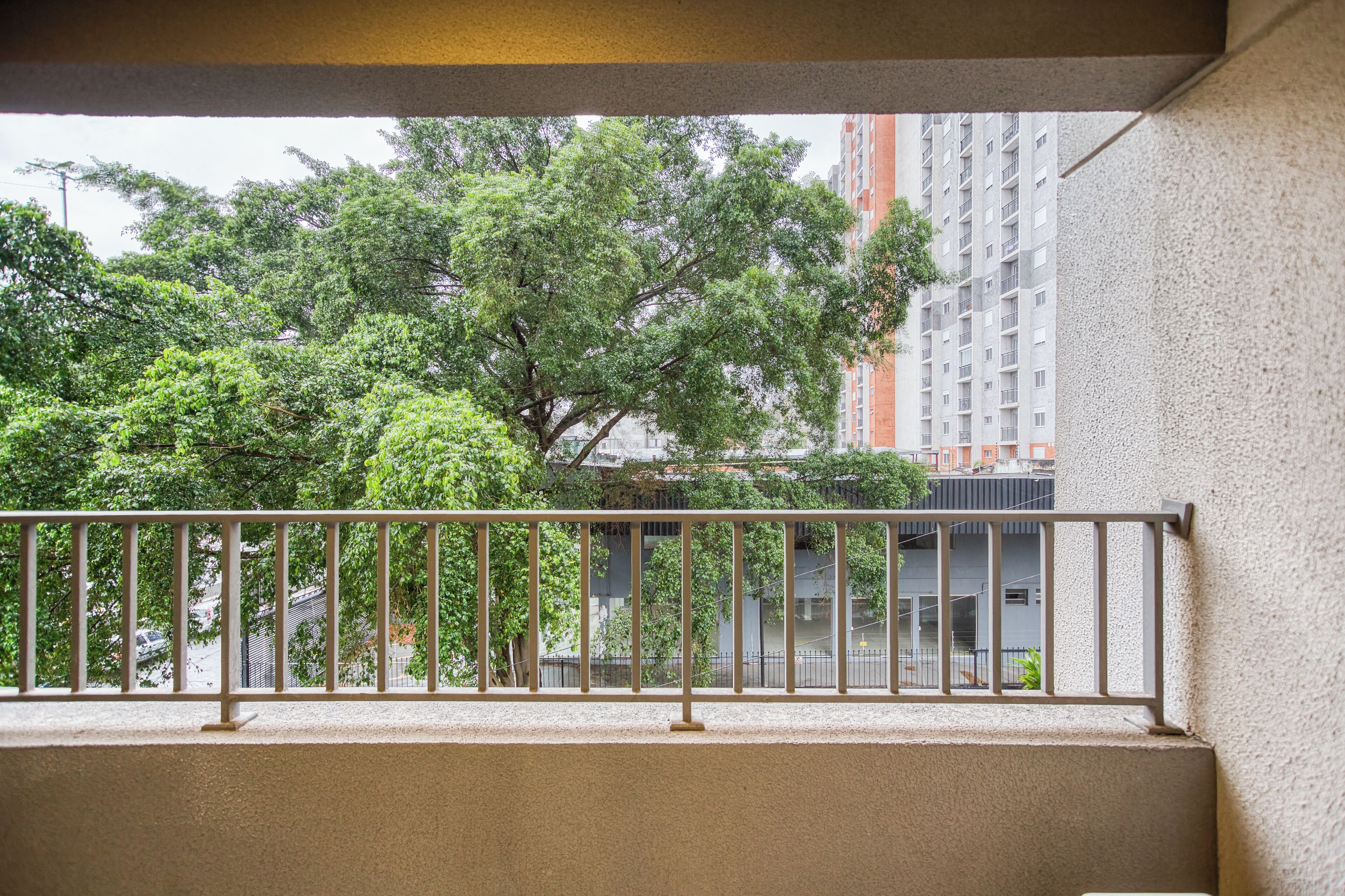 A balcony with a metal railing overlooking a tree and a building.