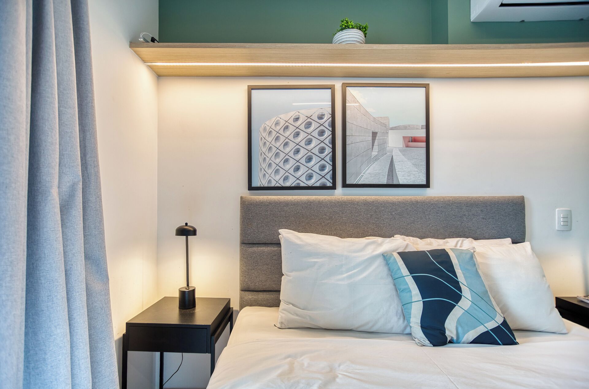 A neatly made bed with white and blue pillows, a grey headboard, and two framed pictures on the wall.