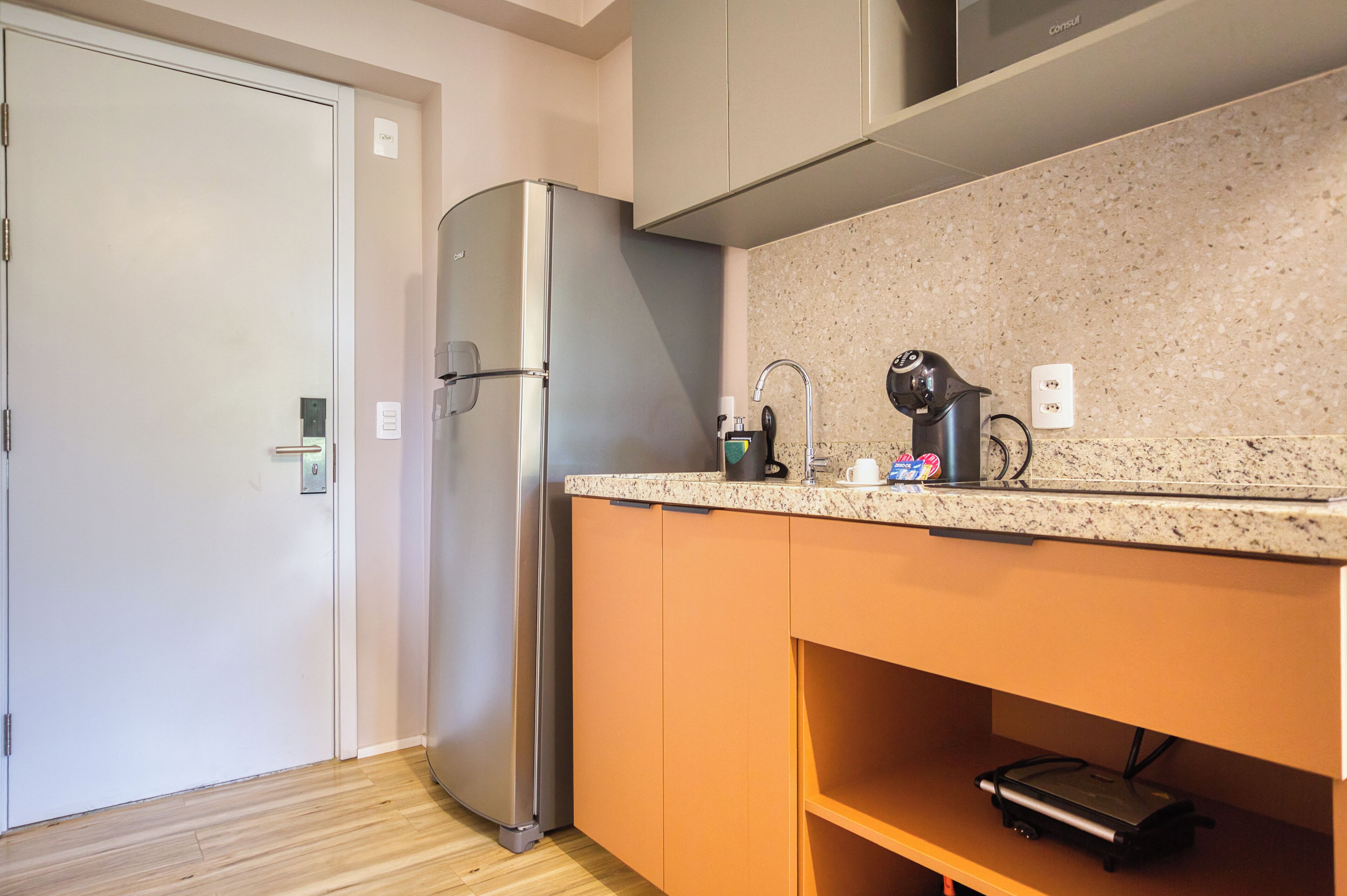 A compact kitchen with a stainless steel refrigerator, a granite countertop, and a built-in oven.
