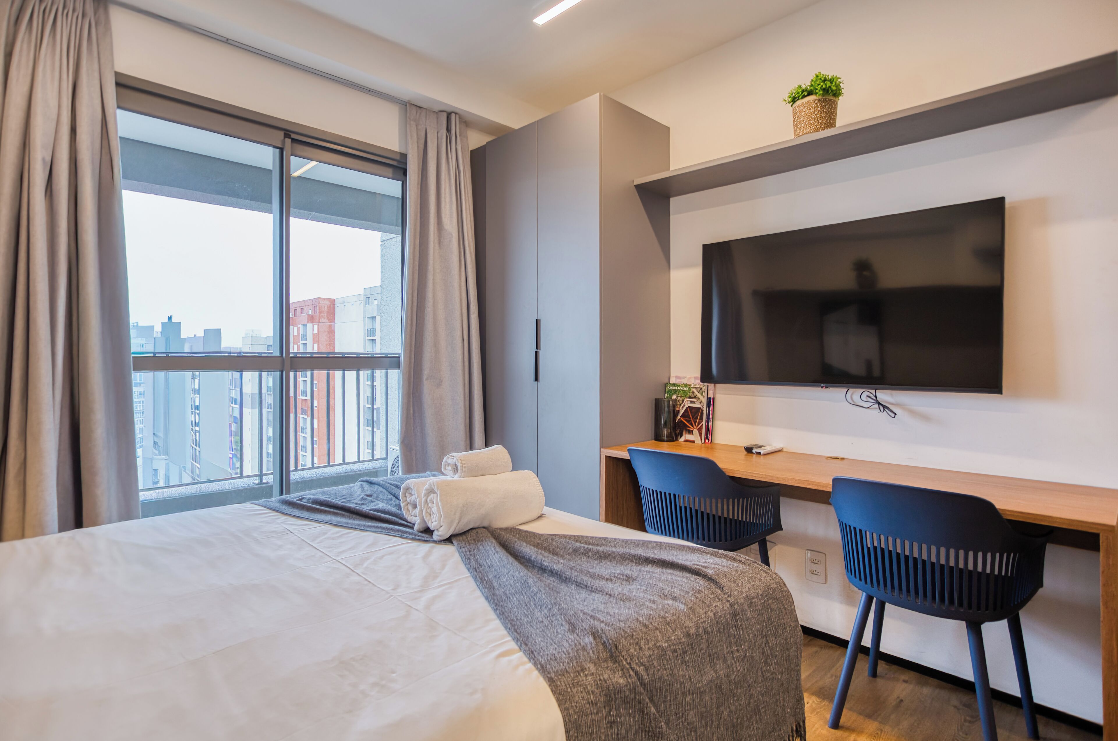 Une chambre d’hôtel moderne dotée d’un grand lit, d’un bureau avec deux chaises, d’une télévision à écran plat et offrant une vue sur la ville.