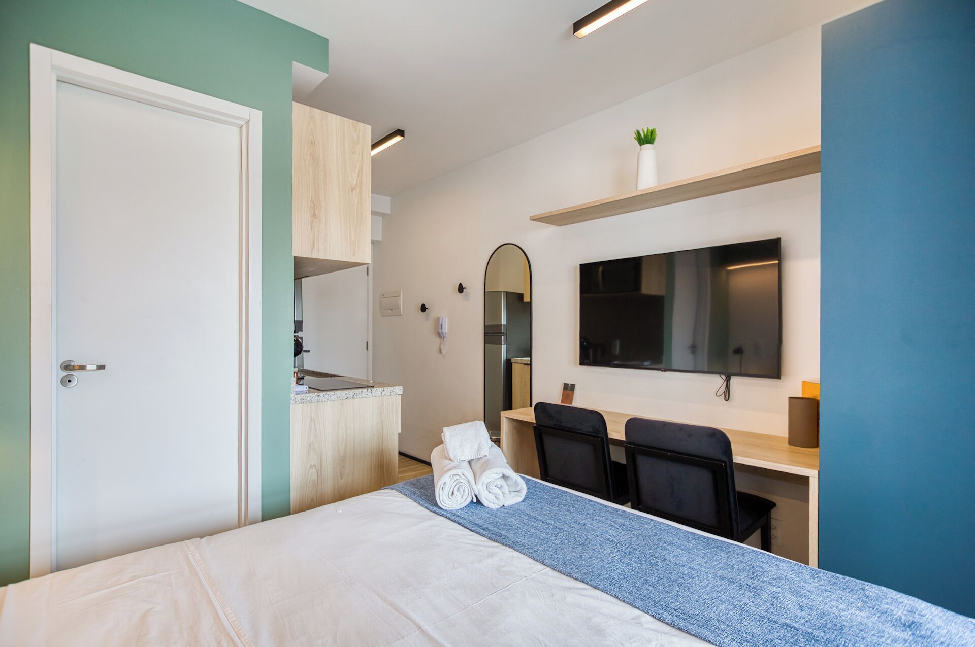 A hotel room with a bed, a desk, a chair, a TV, and a mirror.