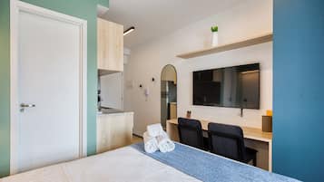 A hotel room with a bed, a desk, a chair, a TV, and a mirror.