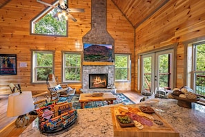 Ein gemütliches Blockhaus-Interieur mit Kamin aus Naturstein, Holzwänden, großen Fenstern und einem Essbereich mit Snacks und Getränken.