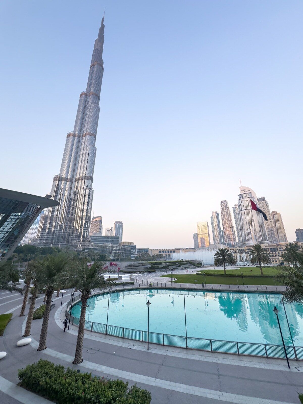 A modern urban landscape with a prominent skyscraper, a large public swimming pool, and a well-maintained park area.