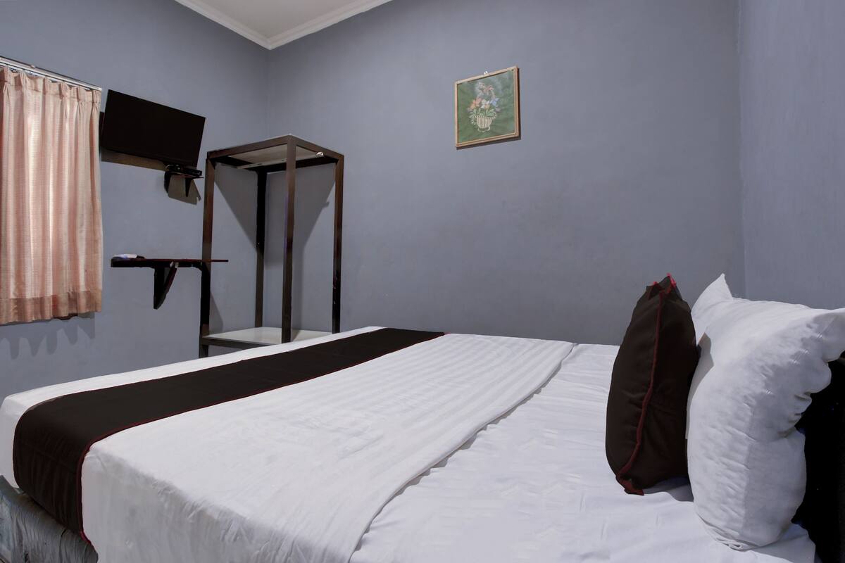 Une chambre d’hôtel avec un lit, un téléviseur fixé au mur, une petite table et une fenêtre avec des rideaux.