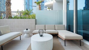 A modern outdoor seating area with a sofa, a round table, and a small table, surrounded by a glass wall and a view of tall buildings. - Keyrock Living - Elegant Studio in Business Bay (Dubai)