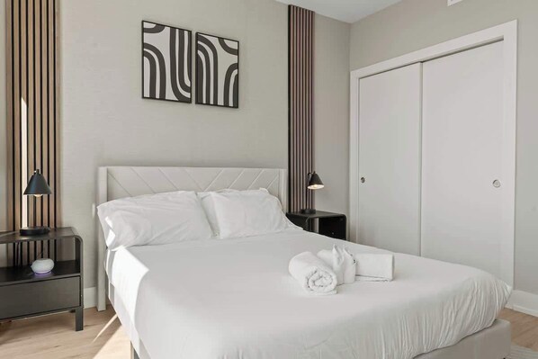 A neatly arranged bedroom with a large bed, a bedside table with a lamp, and a wardrobe.