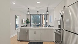 Cocina moderna con electrodomésticos de acero inoxidable, una isla central, iluminación colgante y vistas de la ciudad a través de amplios ventanales.