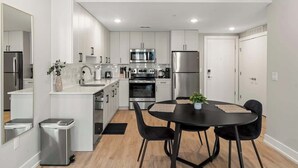 A modern kitchen with white cabinets, stainless steel appliances, and a dining area with a black table and chairs. - Chic 1BR Luxury Apartment in Philly for 4 Guests (Philadelphia)