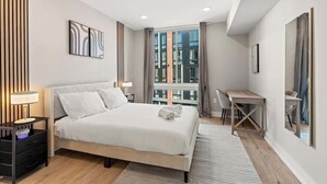 A modern hotel room with a large bed, a desk, and a view of the city through large windows. - Chic 1BR Luxury Apartment in Philly for 4 Guests (Philadelphia)