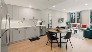 A modern kitchen with white cabinets, a dining area with a round table and chairs, and a living room with a sofa and a TV. - Stylish 1BR Sleeps 4 near Independence Hall (Philadelphia)
