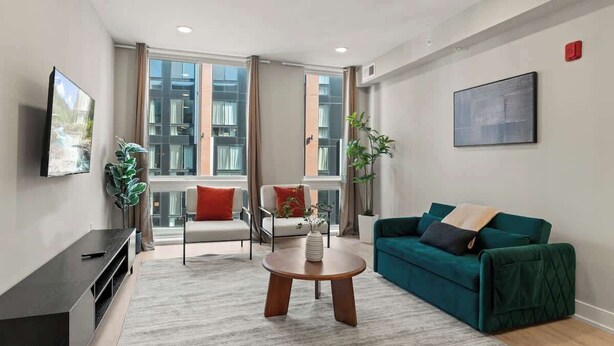 A modern living room with a large window, a green sofa, a white armchair, and a round coffee table. - Stylish 1BR Sleeps 4 near Independence Hall (Philadelphia)