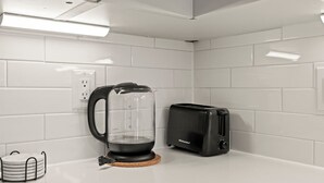 A kitchen with white tiled walls, a coffee maker, a toaster, and a small white appliance on the counter. - Stylish 1BR Sleeps 4 near Independence Hall (Philadelphia)