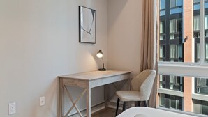 A bedroom with a bed, a desk, and a chair. There is a window with curtains, a wall-mounted light, and a framed picture. - Stylish 1BR Sleeps 4 near Independence Hall (Philadelphia)