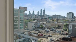 Stadsgezicht met uitzicht op de skyline, waaronder het Chrysler Building, en een parkeerplaats met diverse auto's.