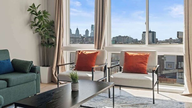 Een moderne woonkamer met uitzicht op de stad, met een bank, fauteuils, een salontafel en een potplant.