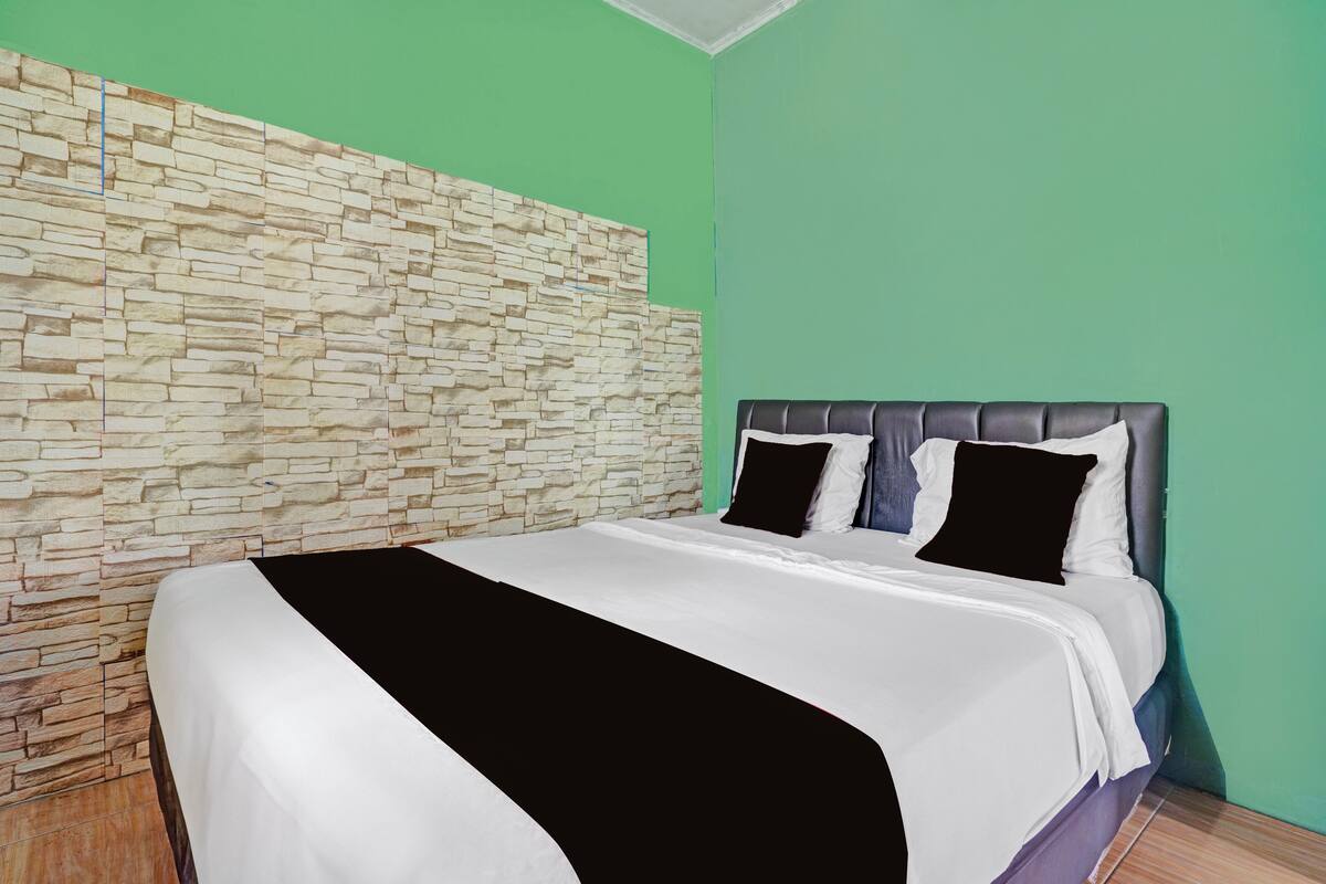 A bedroom with a stone-patterned headboard, a bed with white and black bedding, and green walls.