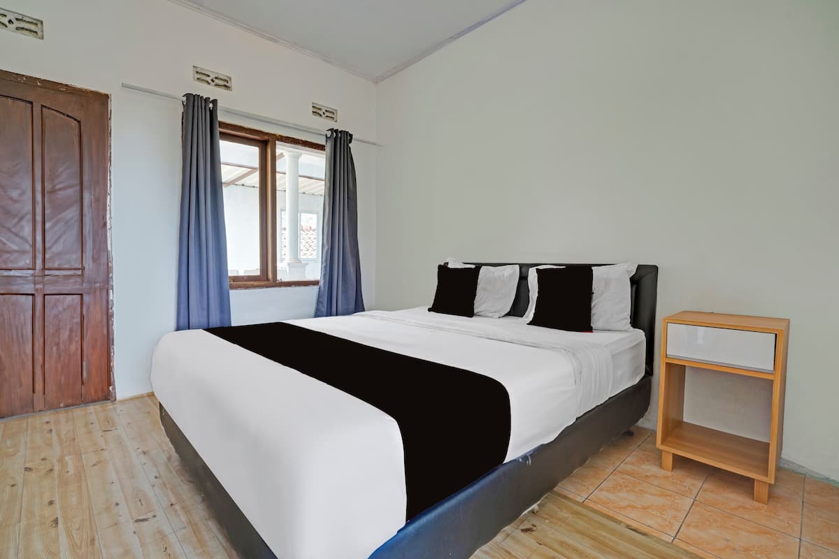 A bedroom with a bed, a wooden nightstand, a window with curtains, and a wooden door.