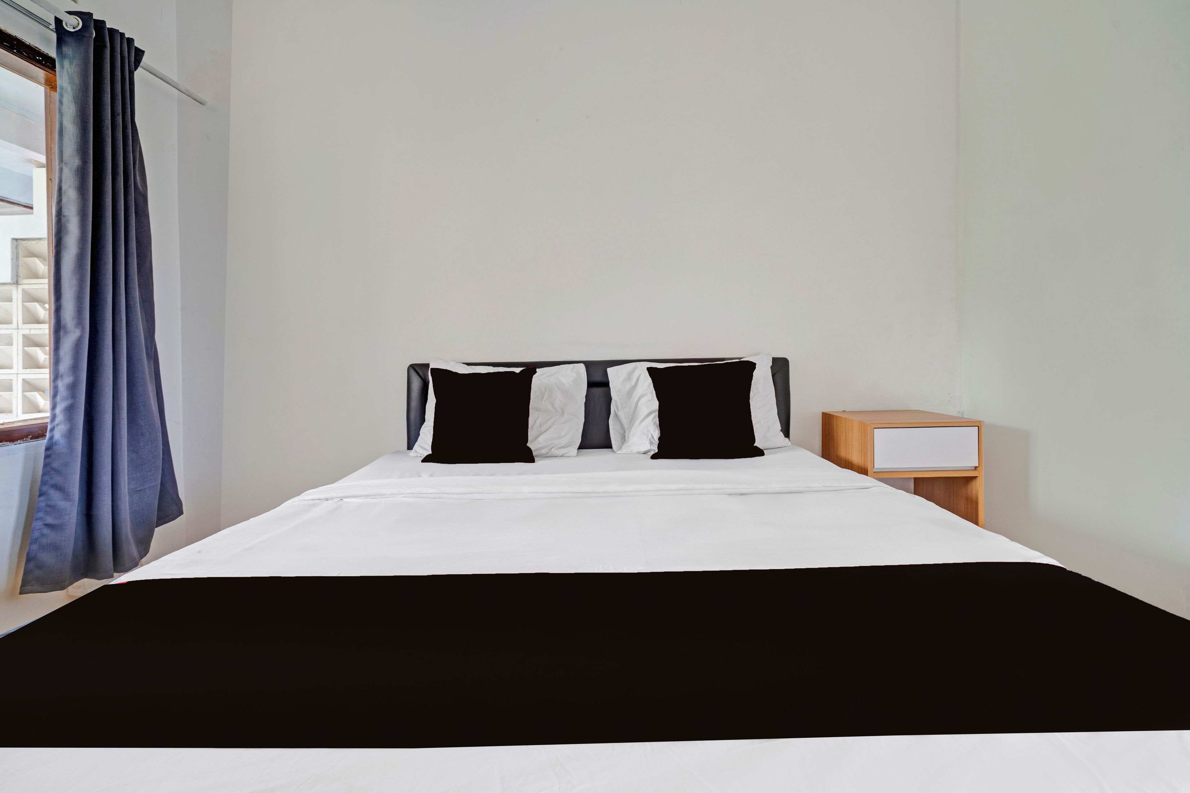 Habitación de hotel con cama, mesita de noche, ventana con cortinas y vistas al exterior.
