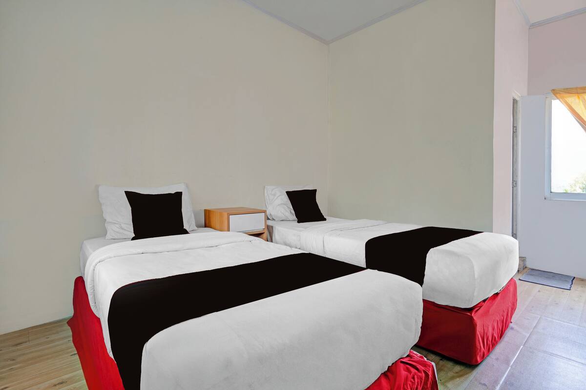 A room with two beds, each with white bedding and black pillows, and red footstools.