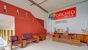 A reception area with a red wall, wooden furniture, and a banner reading "ORCHID VILLA". - Collection O Subang near Ciater Subang formerly Orchid Villa Ciater (Ciater)
