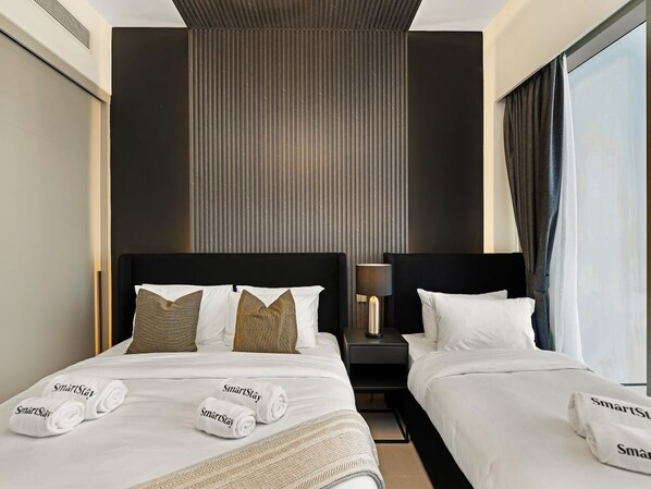 A hotel room with two beds, a nightstand with a lamp, and a large window with curtains.