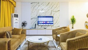 A modern living room with a flat-screen TV, two sofas, a coffee table, and a fan. - Luxurious Abuja Apartment With Modern Amenities (Abuja)